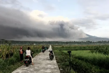 El Monte Semeru arroja materiales volcánicos al aire mientras la gente observa durante una erupción en Lumajang, Java Oriental, Indonesia.