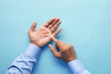 Hombre con mangas azules con pastillas en una mano señalándolas con la otra mano.