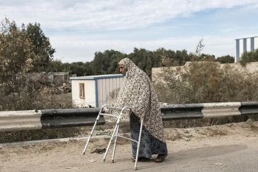 Una mujer palestina que camina con la ayuda de un marco recorre la calle Salah al-Din en Bureij, este sábado, mientras los palestinos evacuan hacia el sur de la Franja de Gaza.