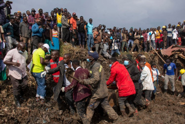 Varias personas llevan a un superviviente a un lugar seguro durante las labores de rescate después de que un deslizamiento de tierra sepultara casas en un vertedero en el distrito de Kiteezi, Kampala, Uganda,