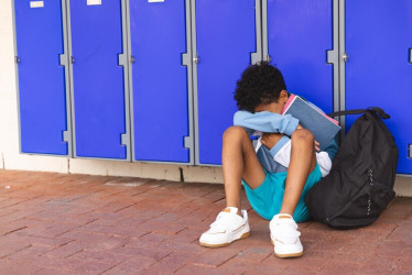 Un niño biracial se sienta solo en la escuela con un espacio para copiar.